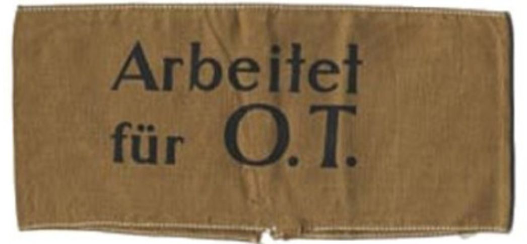 Ein braunes Stück Stoff, welches als Armbinde genutzt wurde. In der Mitte steht in schwarz "Arbeitet für O.T."