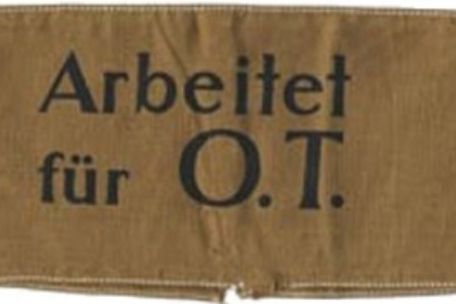 Ein braunes Stück Stoff, welches als Armbinde genutzt wurde. In der Mitte steht in schwarz "Arbeitet für O.T."